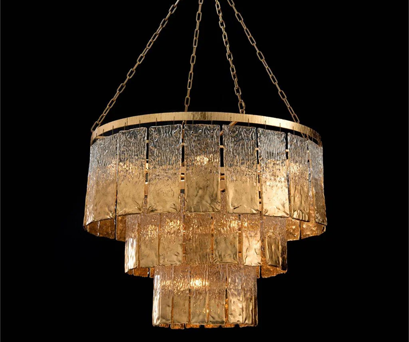 Round, tiered chandelier with glowing amber crystal layers hanging from a gold ring, photographed in a studio against a dark background